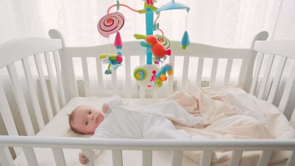Beautiful cute baby boy lying in wooden crib at big window — Stock Video