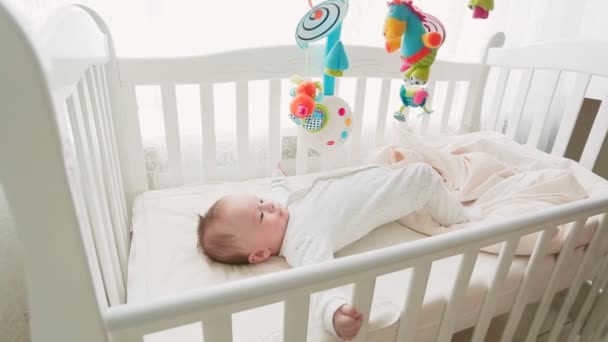 Schattig 3 maanden babyjongen liggend in bedje en kijken naar speelgoed carrousel — Stockvideo