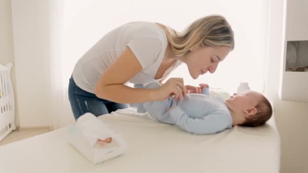 Dolly shot de jeune mère jouant et chatouillant son bébé garçon tout en le déshabillant sur table à langer — Video