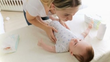 Genç gülümseyen iskambil ile oturma odası masada değiştirilmesi hakkında yalan onun erkek bebek anne. Kamera yakınlaştırır