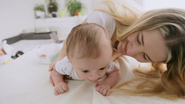 Primer plano de feliz madre joven jugando con su bebé de 3 meses de edad arrastrándose en la cama — Vídeos de Stock