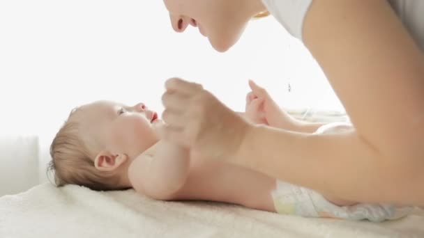 Beautiful young mother kissing her 3 months old baby boy lying on changing table in front of big window — Stock Video