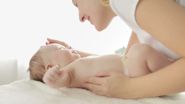 Primer plano de la joven madre acariciando y besando a su bebé acostado en la cama — Vídeos de Stock