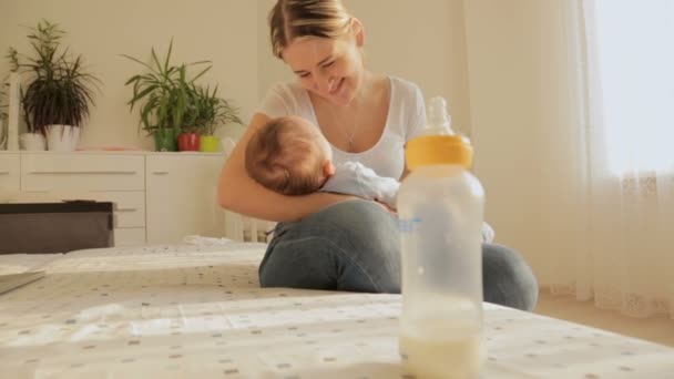Hermosa madre joven sentada en la cama y meciendo a su bebé de 3 meses después de alimentarlo — Vídeo de stock