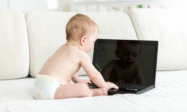 Lindo bebé en pañales sentado en la cama y utilizando el ordenador portátil —  Fotos de Stock