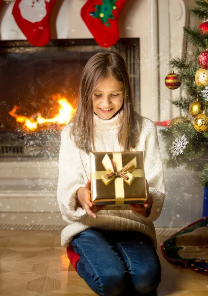 Menina alegre sentado na lareira e abertura de Natal mágico — Fotografia de Stock