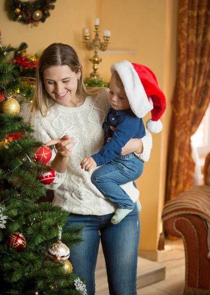 Junge Mutter hält kleinen Jungen in Weihnachtsmütze und dekoriert Christus — Stockfoto