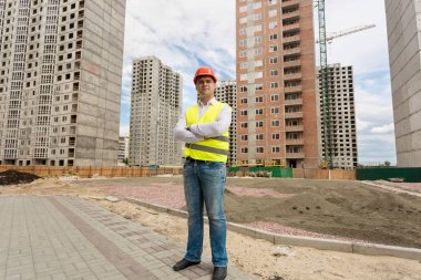 Kask ve güvenlik yeleği site bina duran genç bir işçi