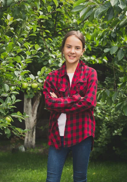 Девочка-подросток в красной клетчатой рубашке позирует в яблоневом саду — стоковое фото
