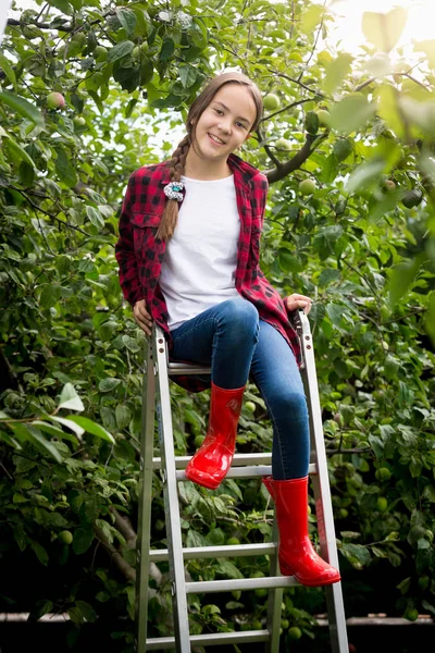年轻女孩在红色惠灵顿靴子坐在梯子在雀鳝 — 图库照片