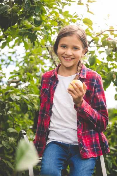 Portrait of smiling girl sitting on stepladder and biting fresh — Stock Photo, Image