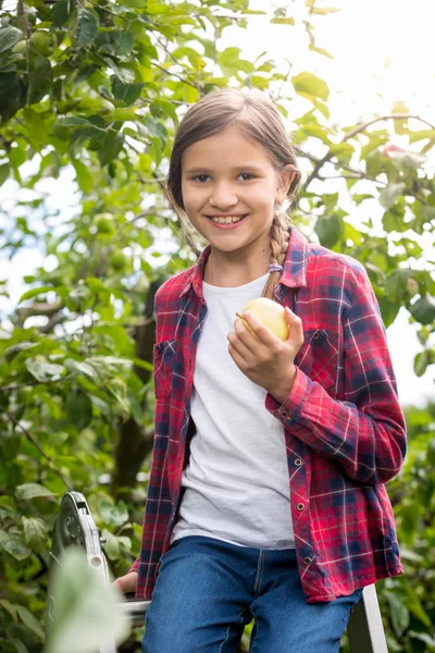 Cute little girl sitting on stepladder at garden and holding fre — Stock Photo, Image