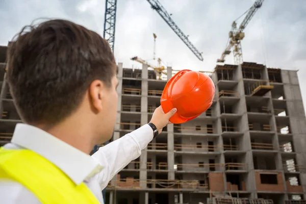 Rear view shot of engineer pointing at building site with red ha