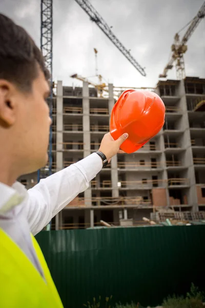 Construction engineer pointing at building site with red hardhat — Stock Photo, Image