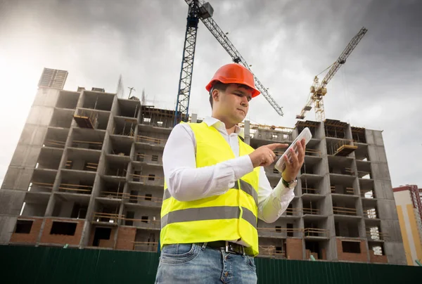 Young architect in hardhat and safety vest using digital tablet — Stock Photo, Image