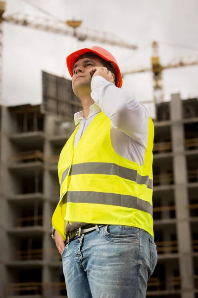 Молодий усміхнений інженер розмовляє по телефону в будівлі під конструктором — стокове фото