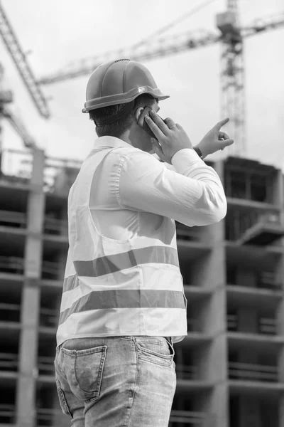 Black and white rear view image of construction engineer talking
