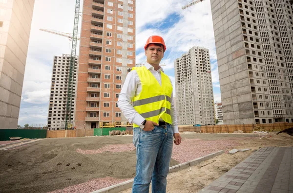 Young man in hardhat and yellow safety vest standing on building — Stock Photo, Image
