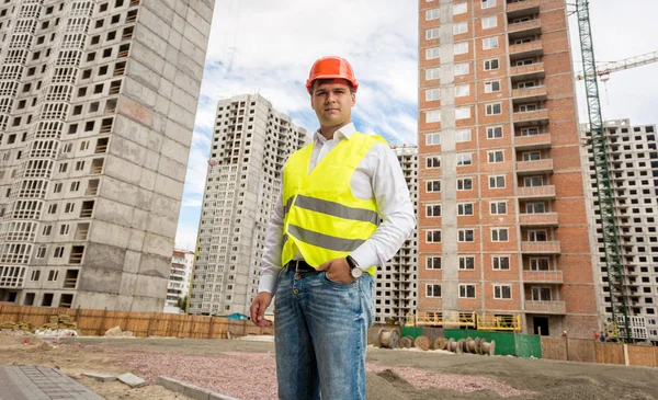 Kask ve güvenlik yeleği buildin karşı poz genç mühendis