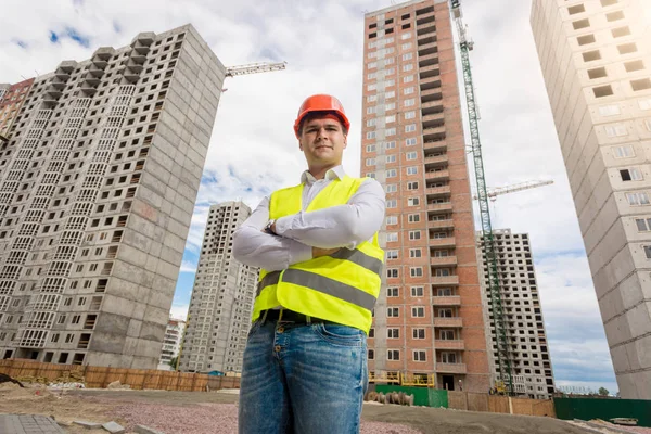 Young architect in hardhat and safety vest posing against new bu — Stock Photo, Image