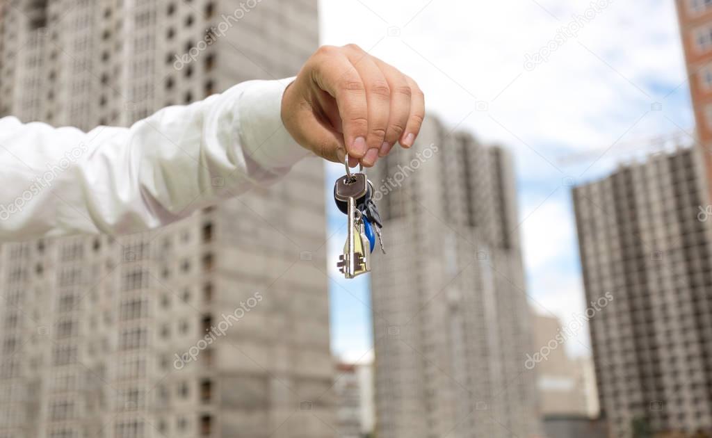 Businessman holding keys from new real estate in hands at buildi