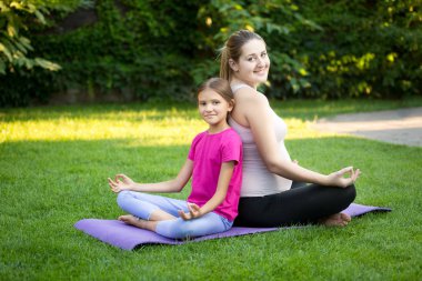 Anne ve gülümseyen kızı pratik yoga ve arka için oturma 