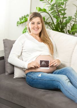 kanepede oturan ve ultrason tutan gülümseyen hamile kadın fe