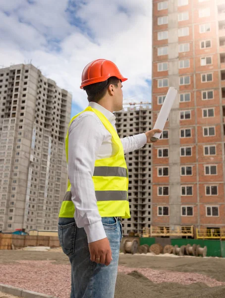 Arquitecto en hardhat apuntando con planos laminados en el edificio —  Fotos de Stock