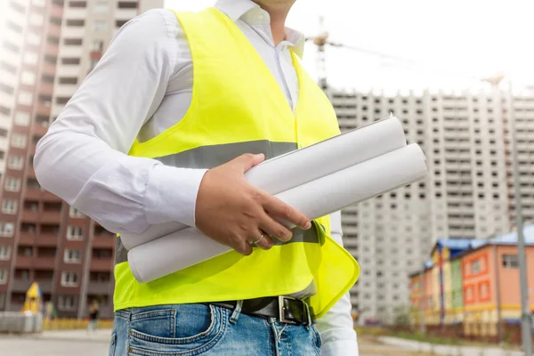 Closeup image of engineer in safety vest holding rolled blueprin — Stock Photo, Image
