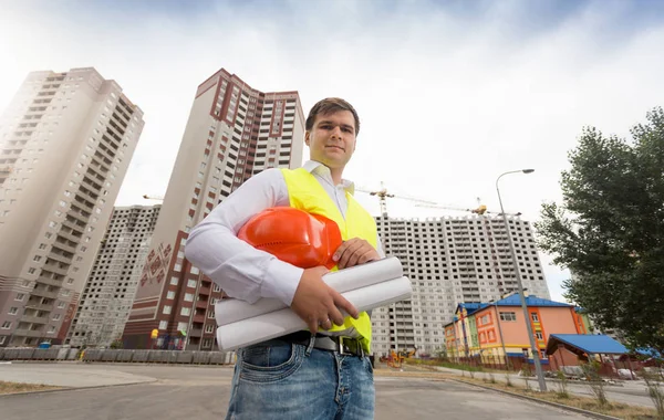 Портрет инженера, стоящего у новых зданий с чертежами — стоковое фото