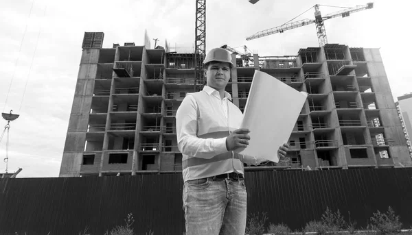 Black and white portrait of young engineer in hardhat with bluep