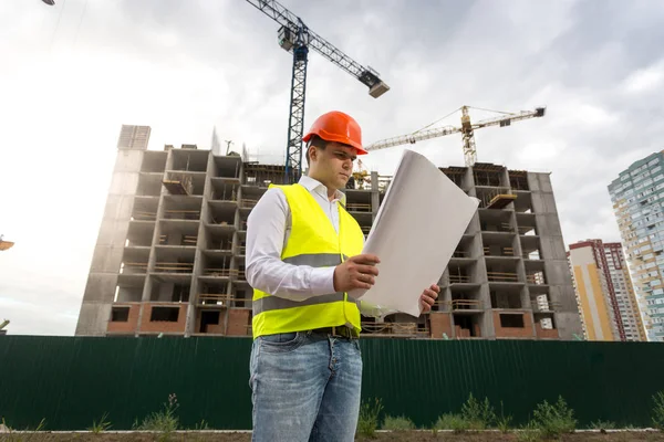 Portrait of young engineer on building site with blueprints — Stock Photo, Image