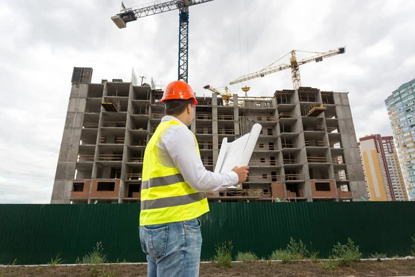 Foreman in hardhat looking on blueprints at building site — Stock Photo, Image
