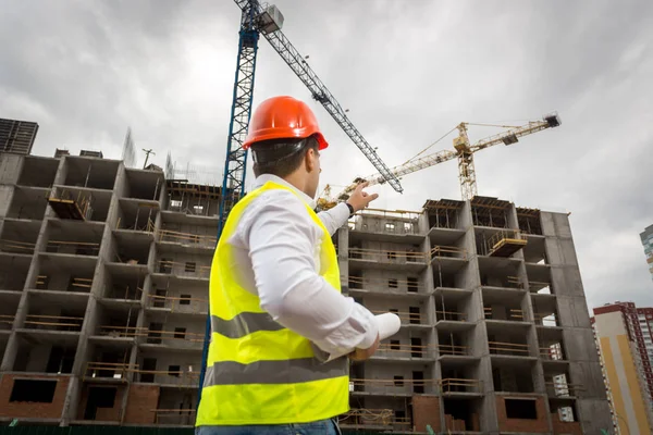 Junge Architektin hält Baupläne in der Hand und zeigt auf Gebäude — Stockfoto