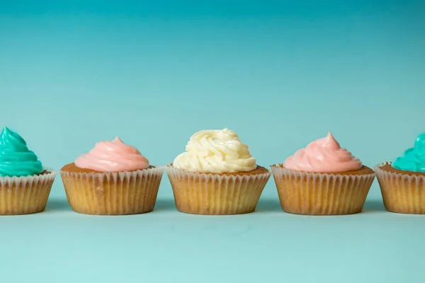 Colorido recém-assado cupcakes em linha sobre fundo azul — Fotografia de Stock