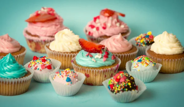 Sabrosos cupcakes recién horneados y dulces de colores sobre turquesa — Foto de Stock