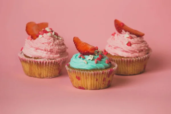 Fechar de três cupcakes com morango sobre fundo rosa — Fotografia de Stock