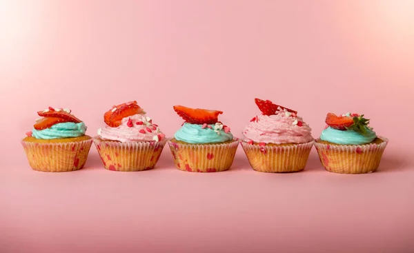 Fila de cupcakes rosados y azules con fresa fresca en la espalda rosada — Foto de Stock