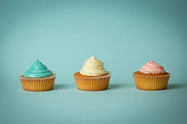 Primer plano de cupcakes con crema de mantequilla de colores sobre fondo azul — Foto de Stock