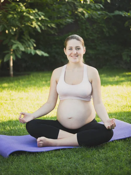 Zâmbind o femeie însărcinată care practică yoga pe iarbă în parc — Fotografie, imagine de stoc