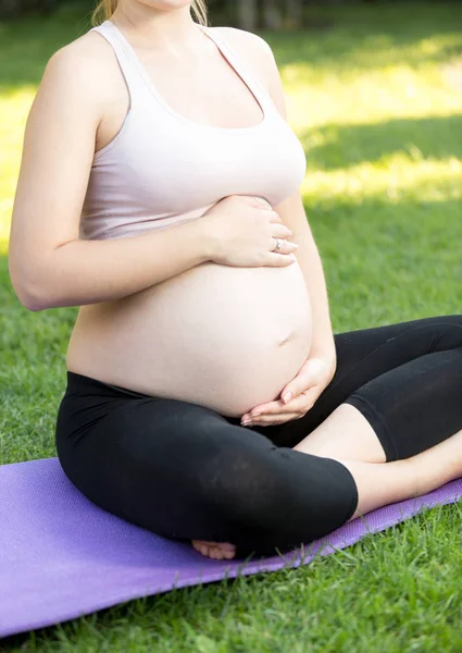 Foto close-up da mulher grávida ativa sentada na grama e touc — Fotografia de Stock