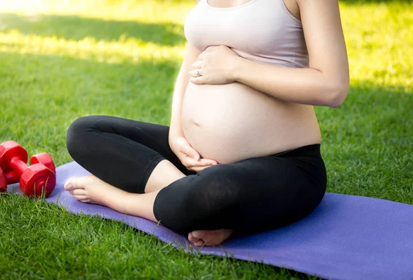 Donna incinta attiva seduta sull'erba al parco e toccante grande — Foto Stock