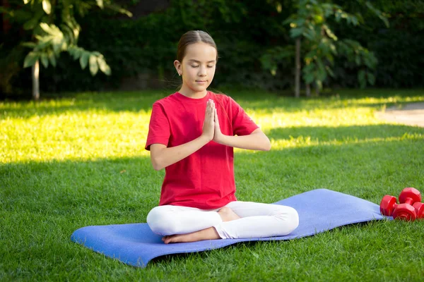 Menina adolescente bonita praticando ioga no tapete de fitness no parque — Fotografia de Stock