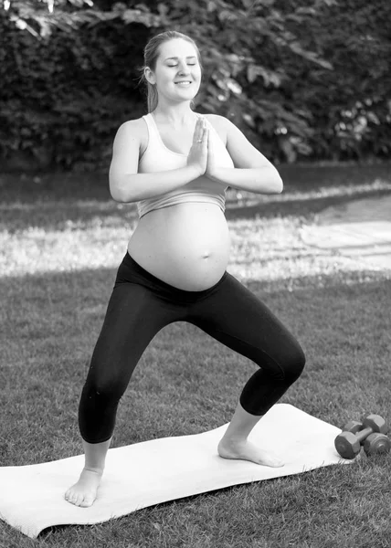Svart och vitt skott av gravid kvinna praktisera yoga på park — Stockfoto