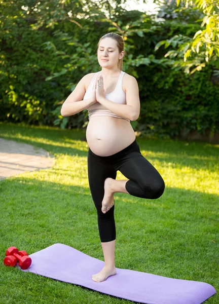 Unga gravid kvinna gör yoga träning på gräs — Stockfoto