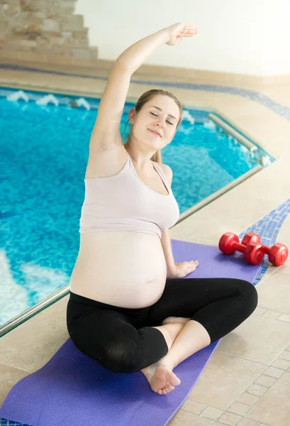 Giovane donna incinta in posa sul tappeto fitness blu in piscina — Foto Stock