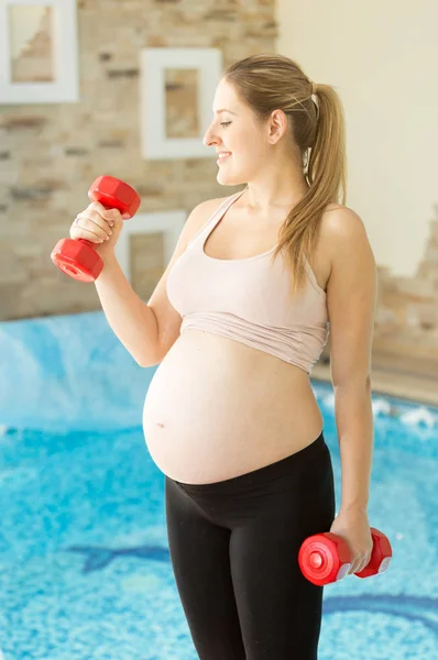 Spor salonunda dumbbells ile poz gülümseyen hamile kadın portresi — Stok fotoğraf