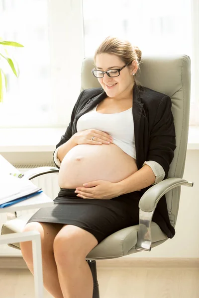 Smiling pregnant woman posing on chair at office — Stock Photo, Image