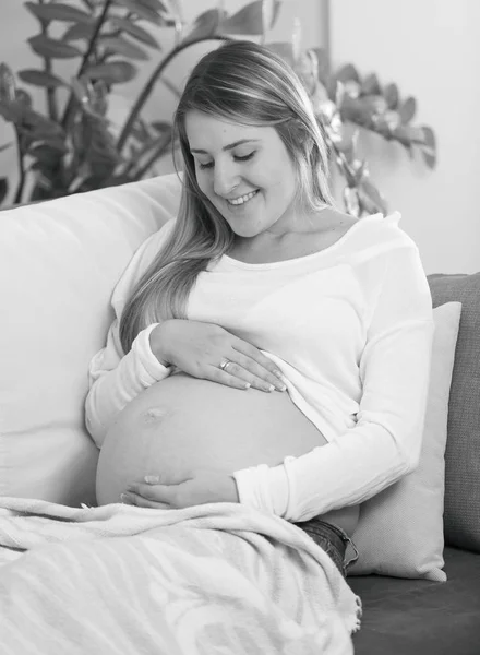 소파에 누워 웃는 임신한 여자의 흑백 초상화 — 스톡 사진