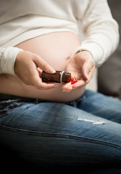 Беременная женщина принимает витамины в таблетках из стеклянной бутылки — стоковое фото